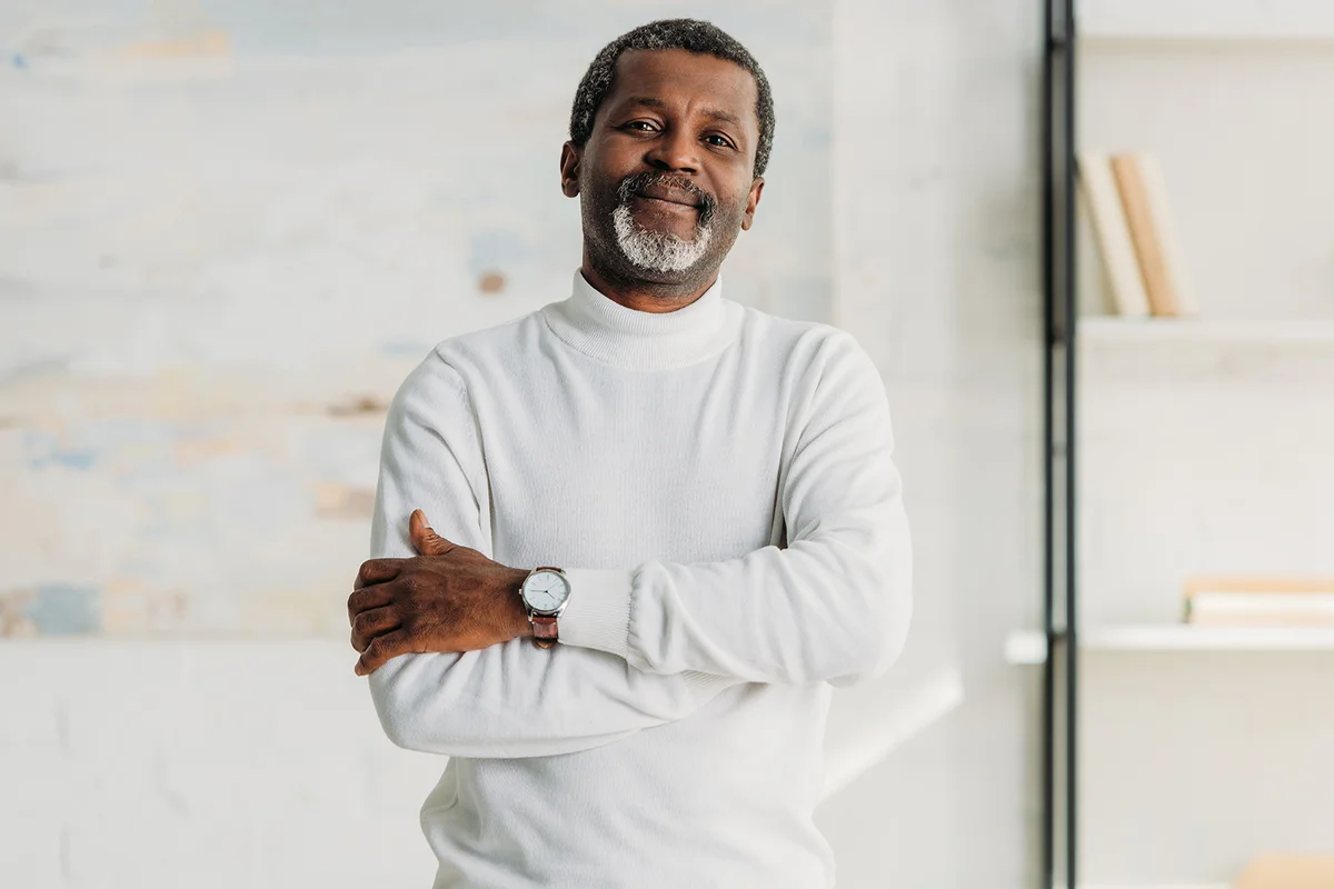 stylish african american man standing with crossed arms and smiling at camera