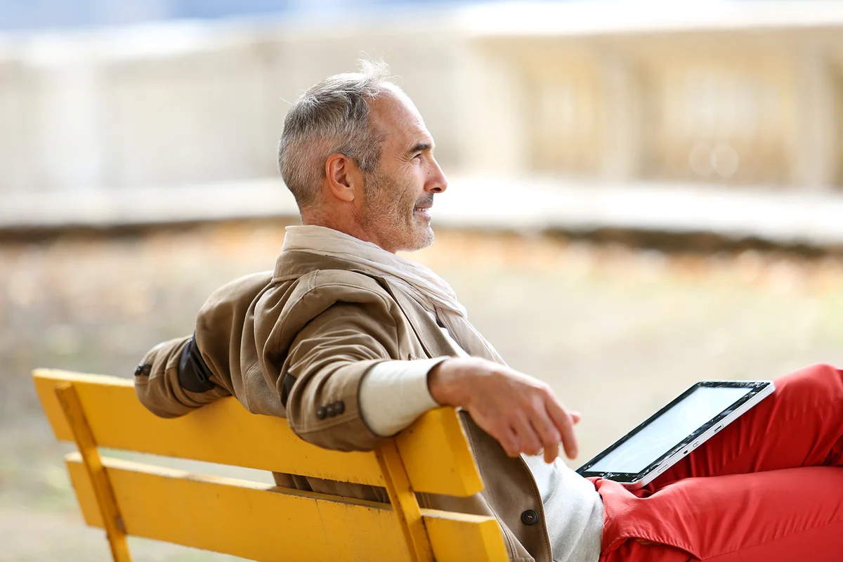 Trendy senior man relaxing on bench with tablet