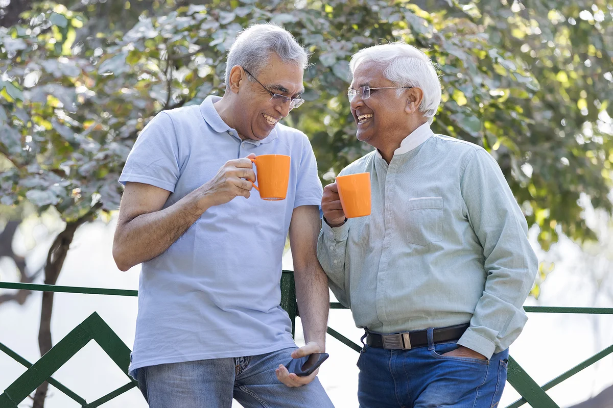 Two old male friends having fun raising a toast with coffee cups at park