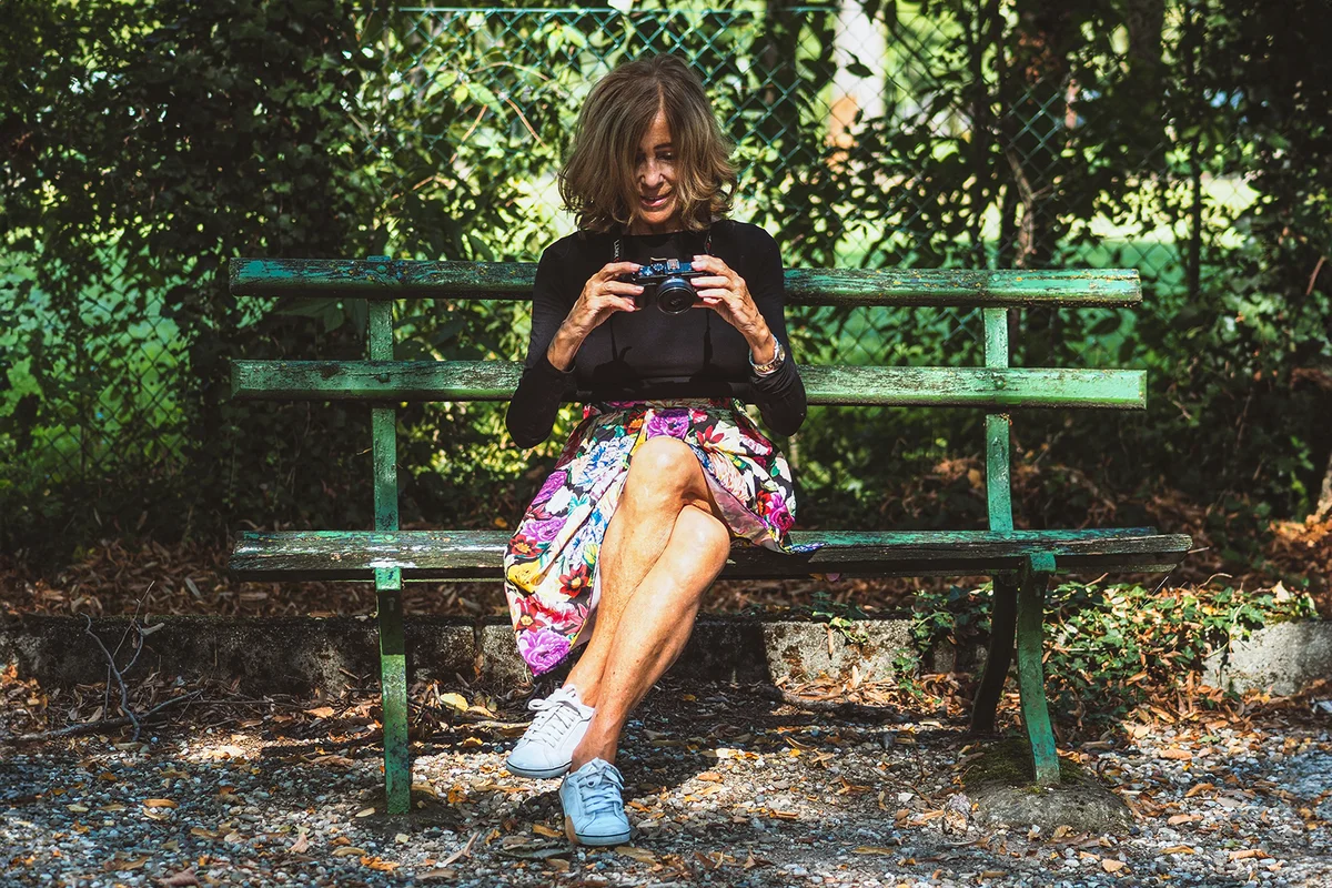 caucasian 70s senior fit happy lady relax with photo camera in park wear floral skirt and black long sleeve shirt