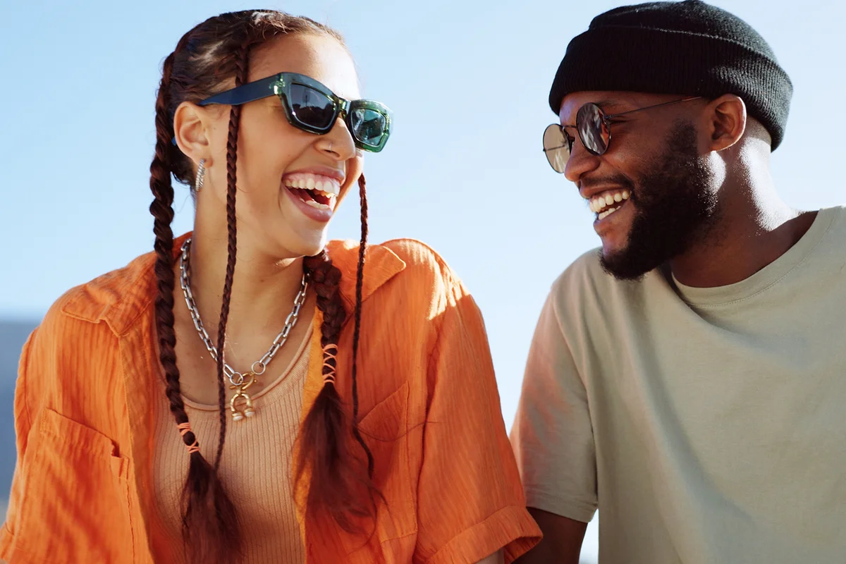 couple with sunglasses in city sitting on building rooftop laughing