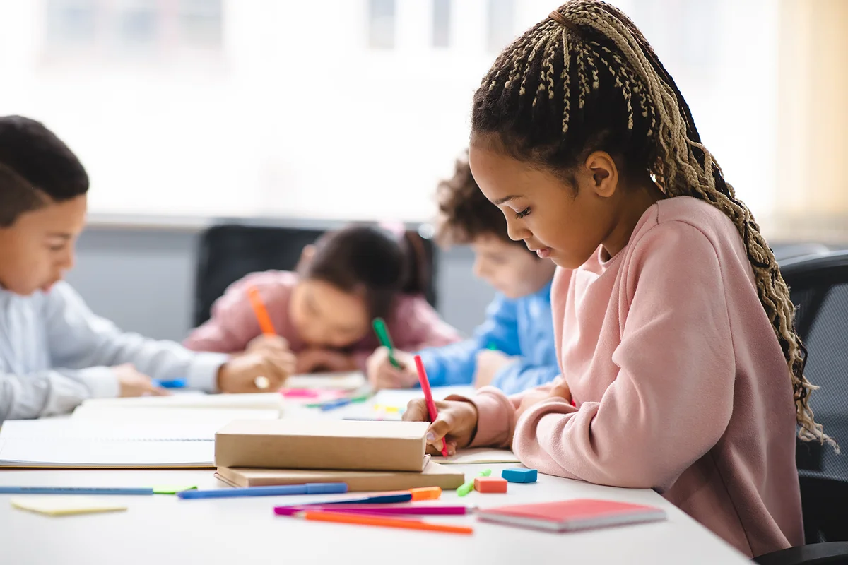 Girl in classroom at primary school or kindergarten, writing