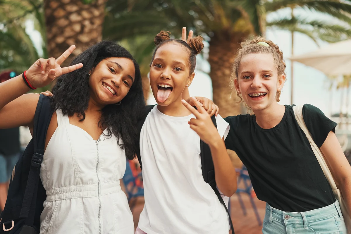 Three girls friends teenagers standing on the street smiling, hugging each other making faces for the camera
