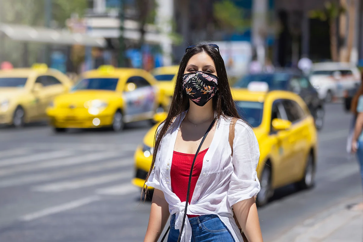 A tourist woman wearing a cloth face mask walks on the busy streets