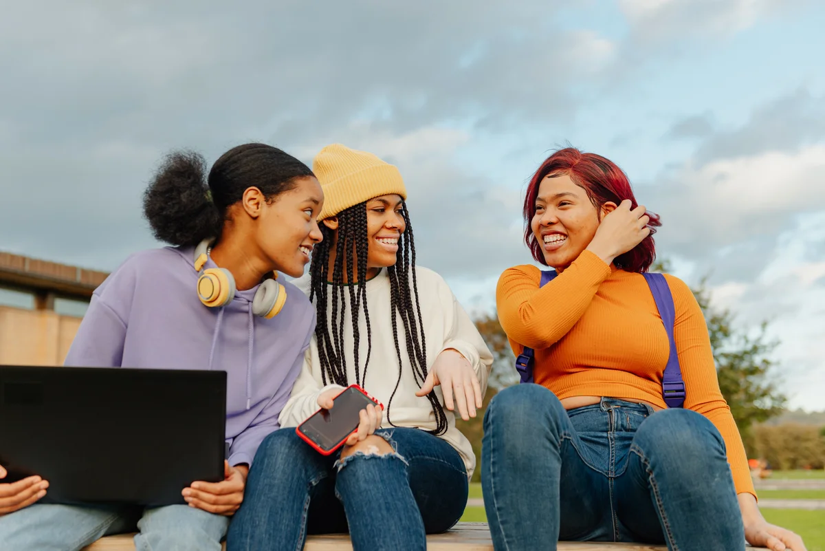 three teenage girls chatting happily sitting on a bench