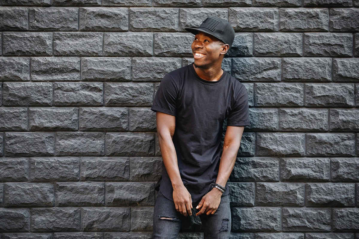 man in black t-shirt standing against brick wall