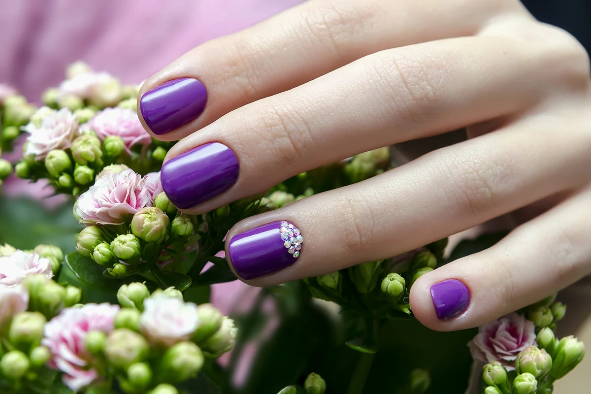 Female hand with sparkle purple nail design and pink flower