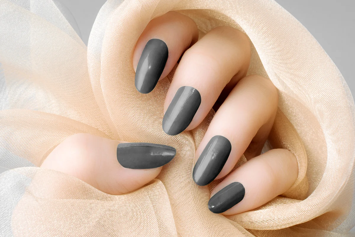Female hand with dark gray nails is holding beige textile, nail care and manicure concept.