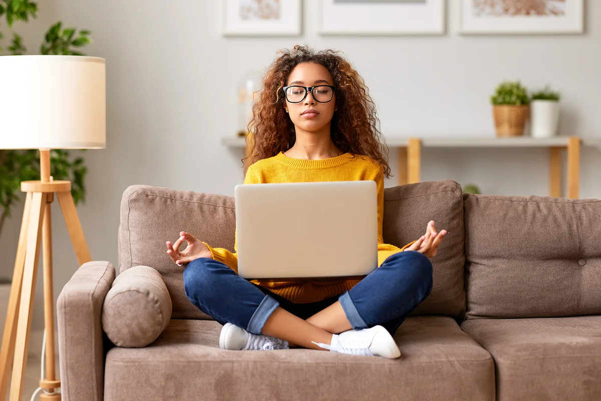 teenage girl sitting with laptop on couch and meditating