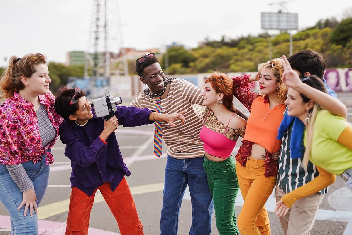 Group of multiracial young people having fun together outdoor while using vintage video camera