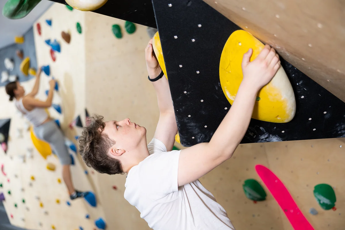 Teenage boy is mastering climbing on training wall in gym