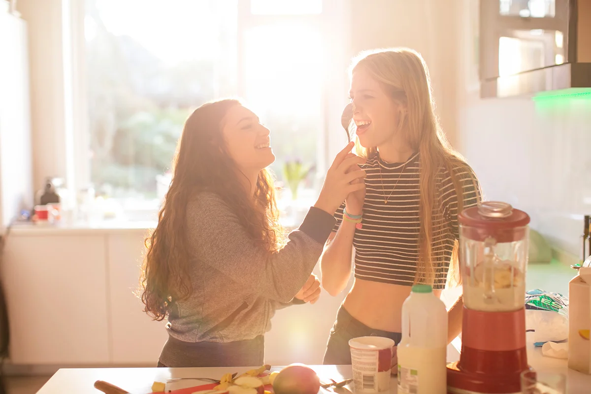Teenage girls playing with spoon in sunny kitchen