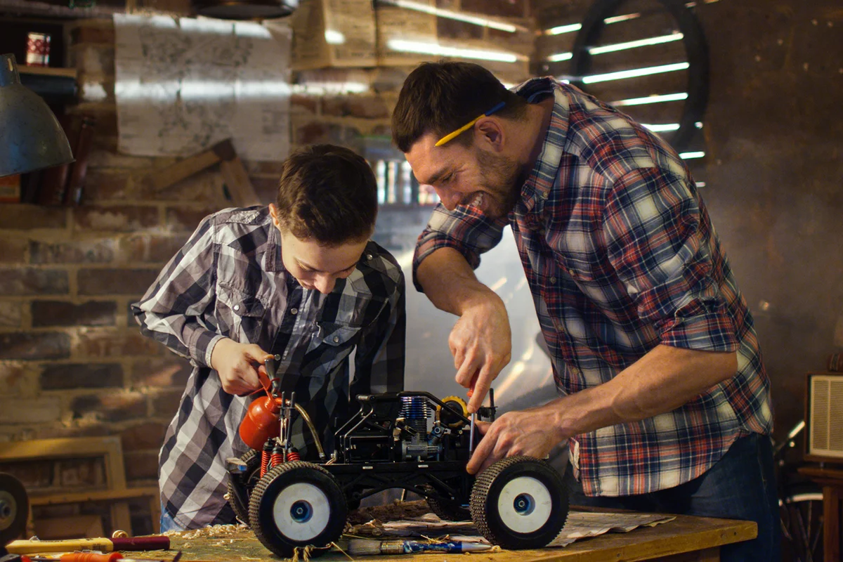 Father and son are working on a radio control toy car in a garage at home.