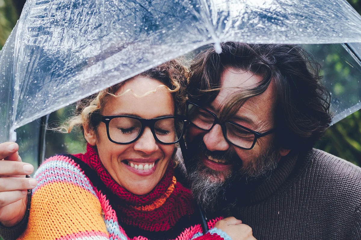 man and woman having fun together under a transparent umbrella in rainy day