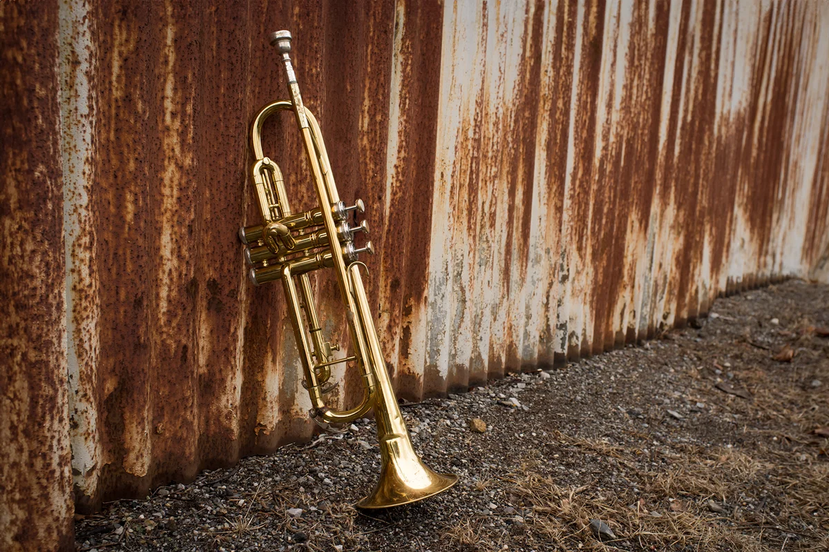 Old worn trumpet stands alone against a grungy rusty fence