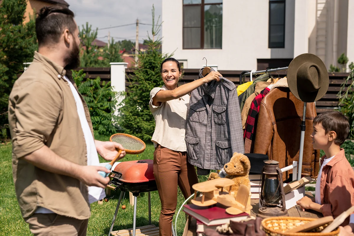 woman holding jacket on hanger and offering to buy it to husband at summer garage sale
