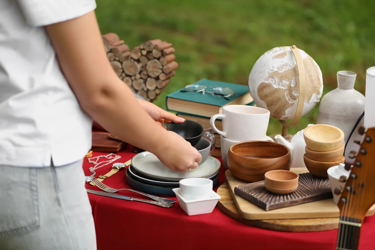 Woman holding beautiful bowls near table with different items on garage sale