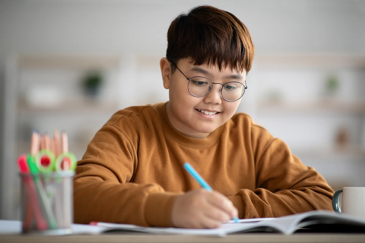 teen boy writing at notebook