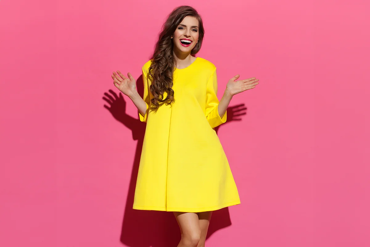 woman with curly long brown hair posing in yellow dress