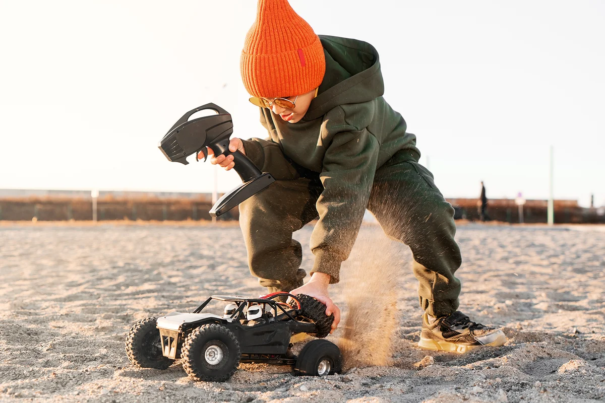 Boy kid playing radio control car riding on sand