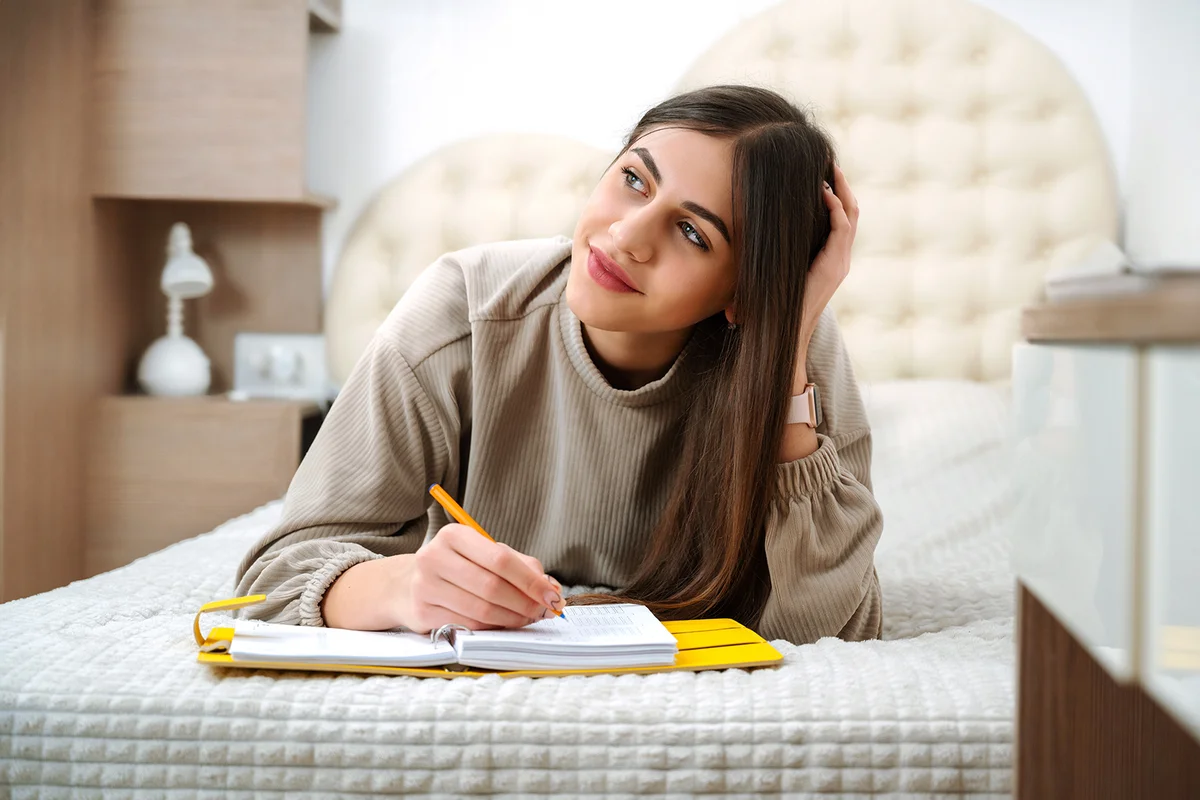 Teen girl lies on the bed and writes in a notebook