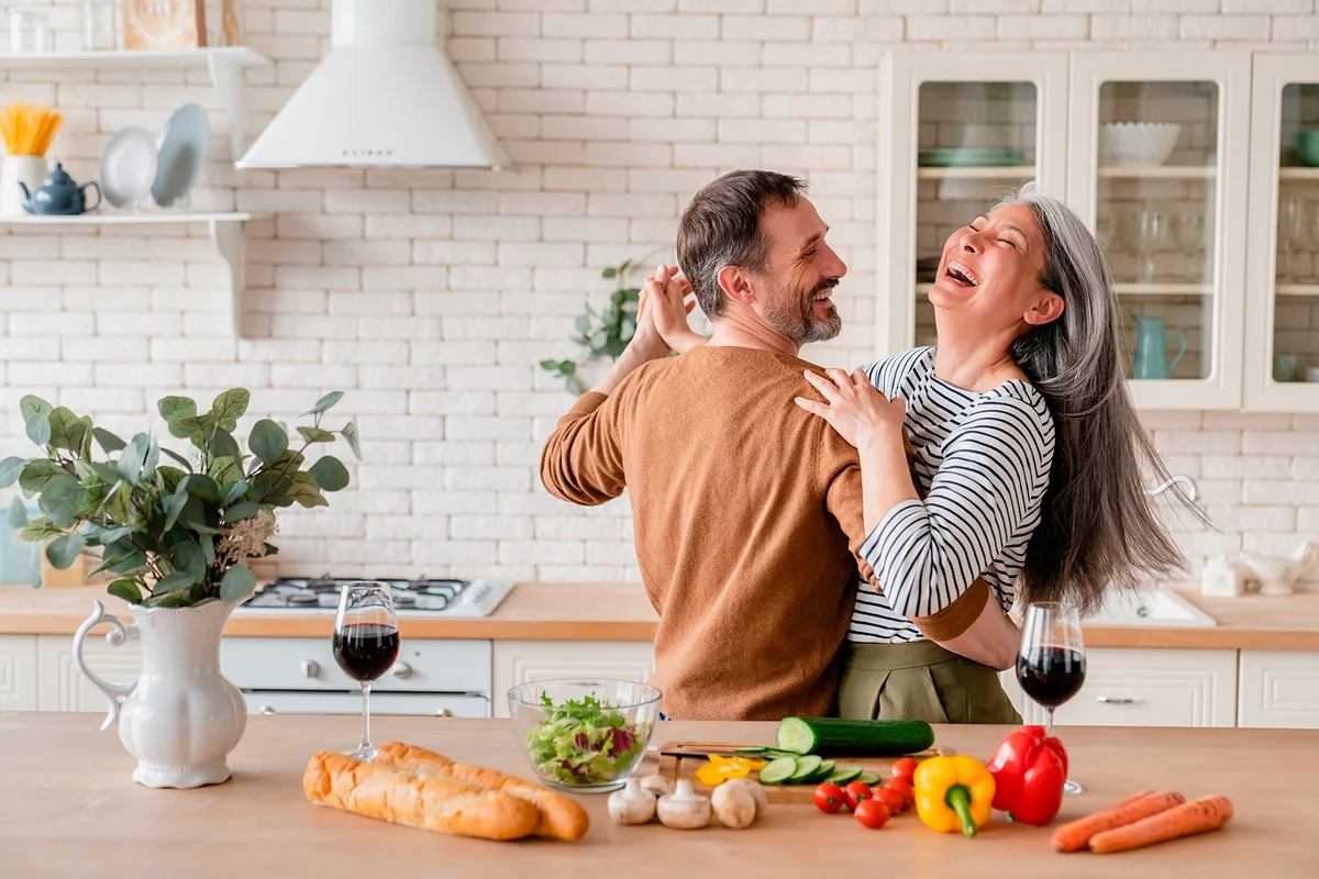 Happy cheerful middle-aged mature couple family parents dancing together in the kitchen, preparing cooking food meal for romantic dinner, spending time together. Active seniors