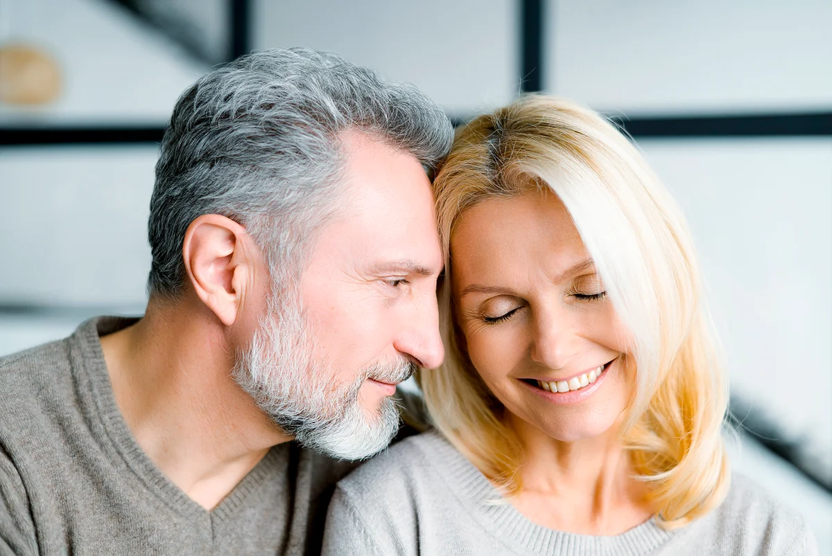 Headshot of romantic middle-aged couple indoors. Handsome grey-haired mature man watching with passion and love at beautiful charming mid-age woman. Mature spouses at home
