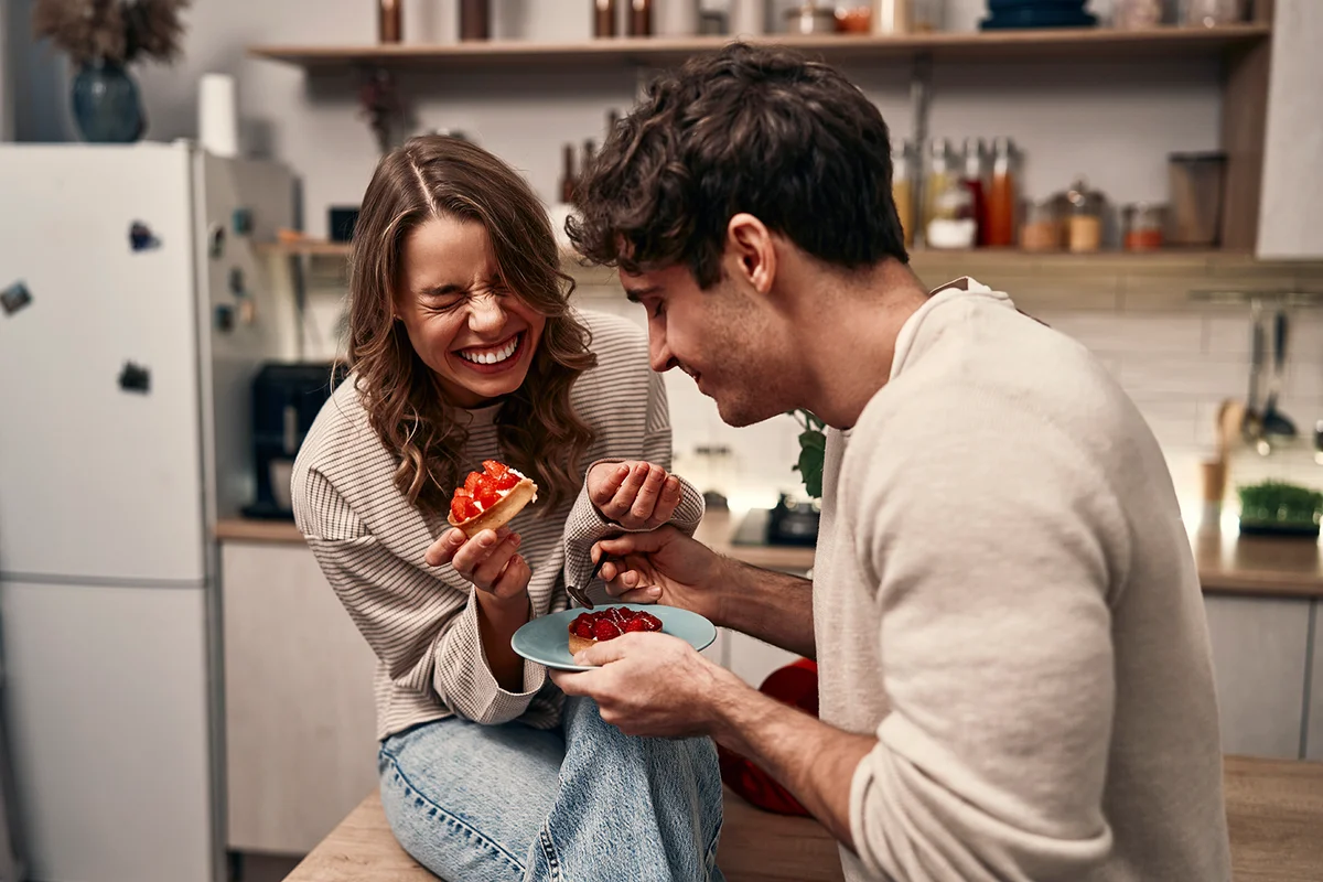 Happy Valentine's Day. Young couple in love eating cakes while sitting on the table in the kitchen, romantically spending the evening together.