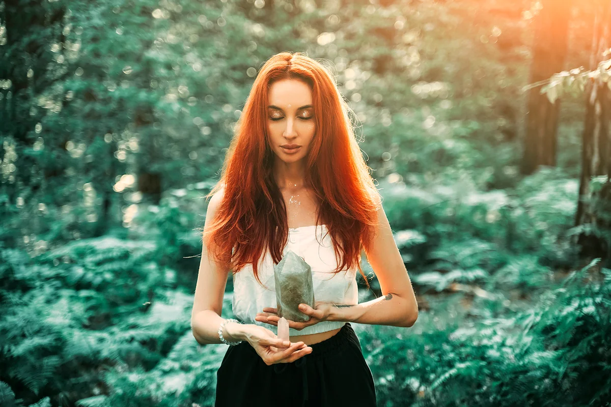 Red-haired beautiful woman holding magic crystal pink quartz. Meditation Spiritual Forest Background