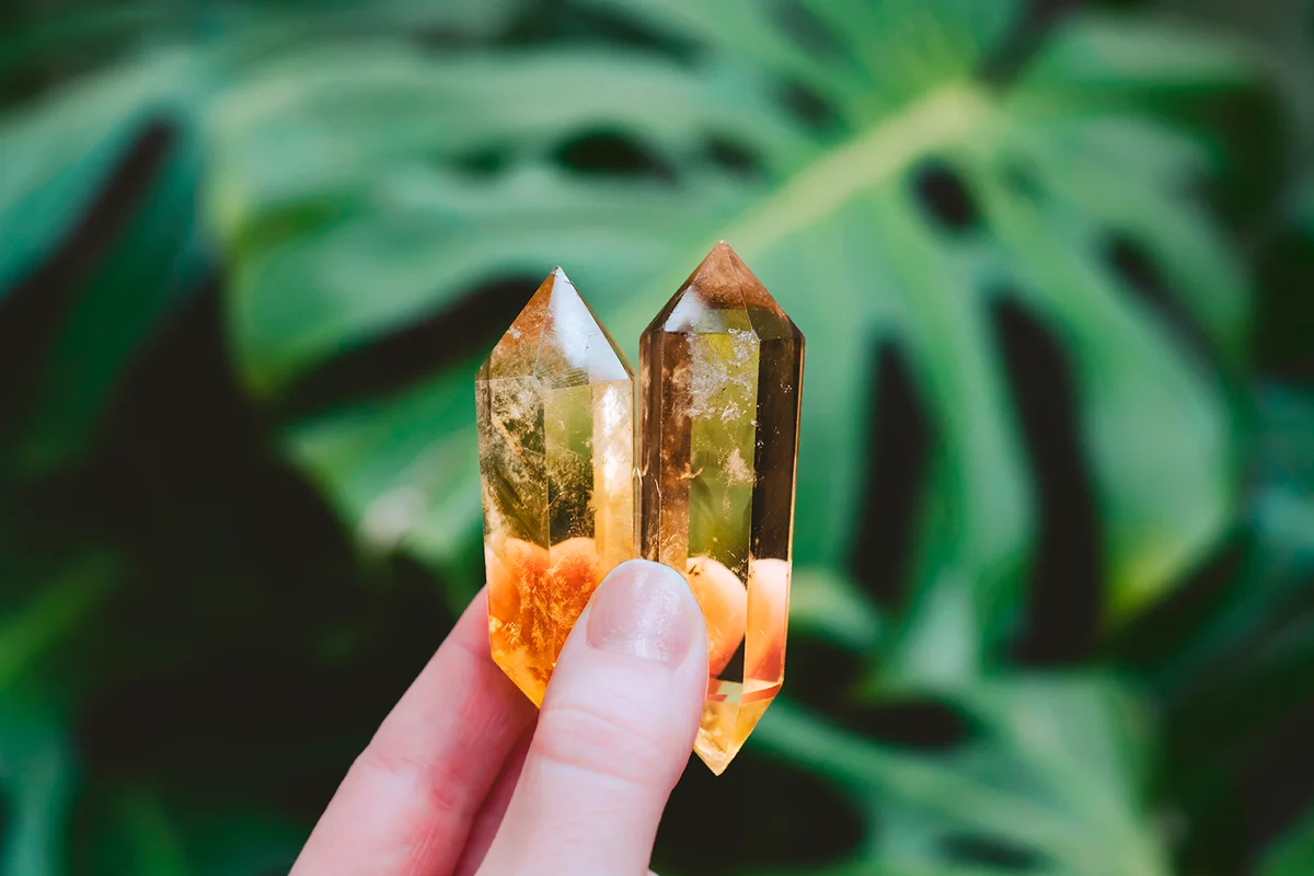 Holding crystals in forest with monstera plants. Citrine crystal points