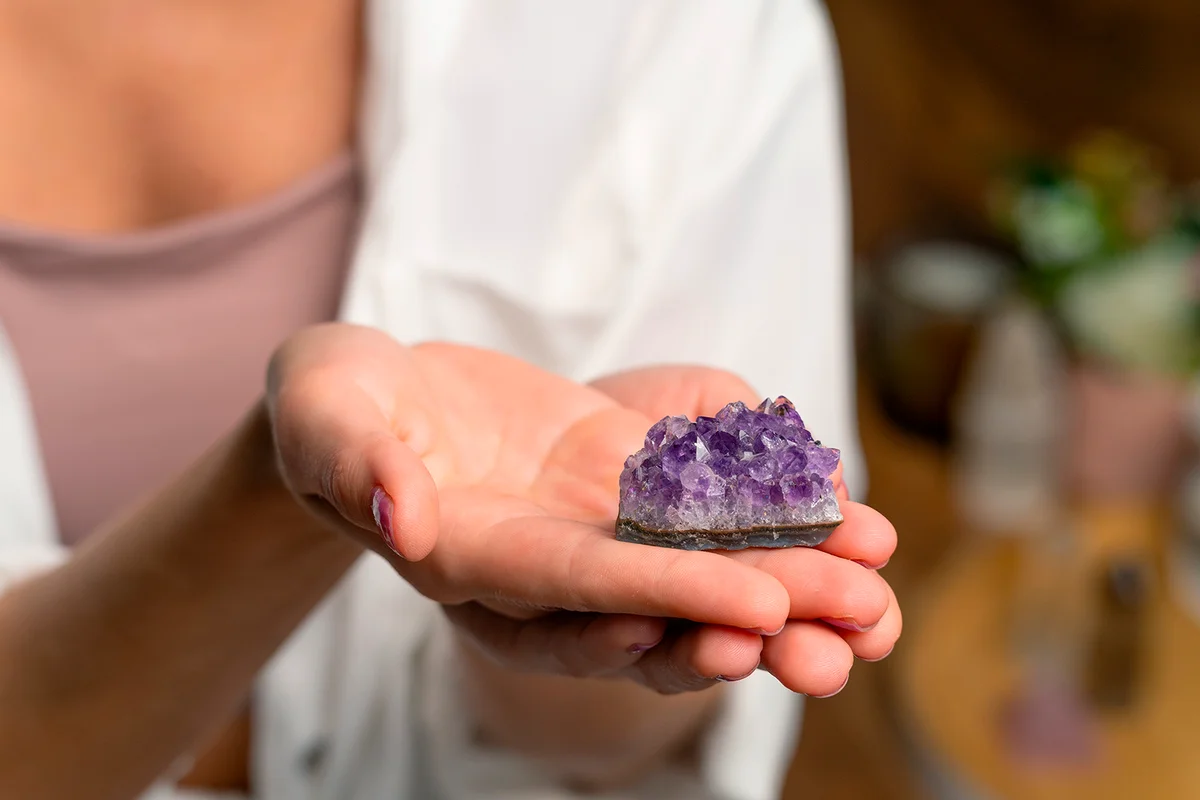 Woman’s hands holding a raw amethyst crystal. Crystal healing, spirituality concept.
