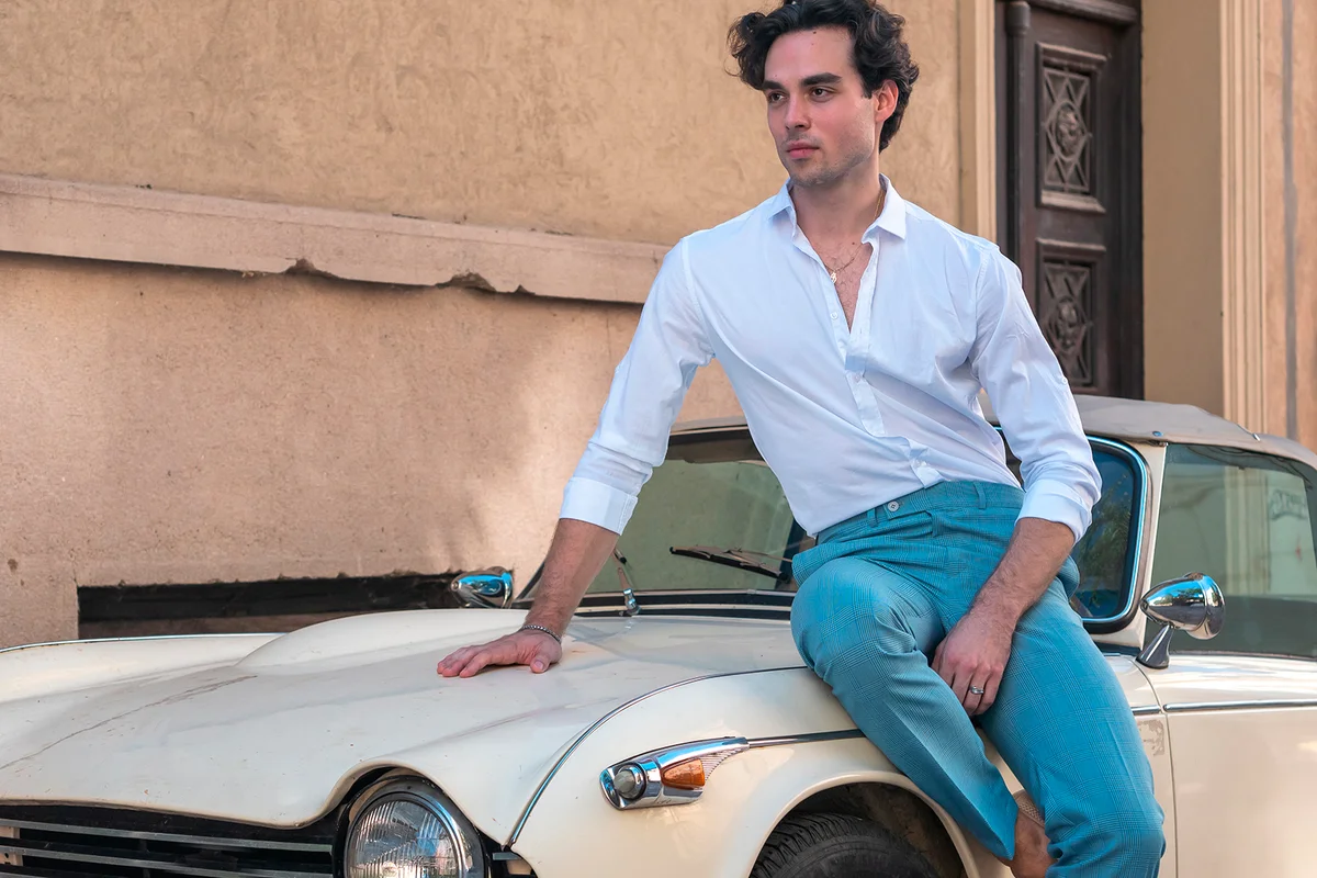 Attractive, handsome man leaning on a retro car in a white shirt. Mediterranean vibe, vintage car