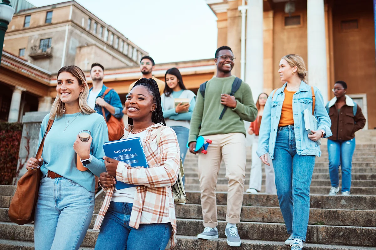Diversity, students and walking on university steps, school stairs or college campus to morning class. Smile, happy people and bonding education friends in global scholarship opportunity or open day
