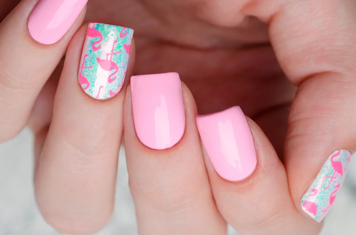 pink manicure with a print of pink flamingos on a gray wooden background