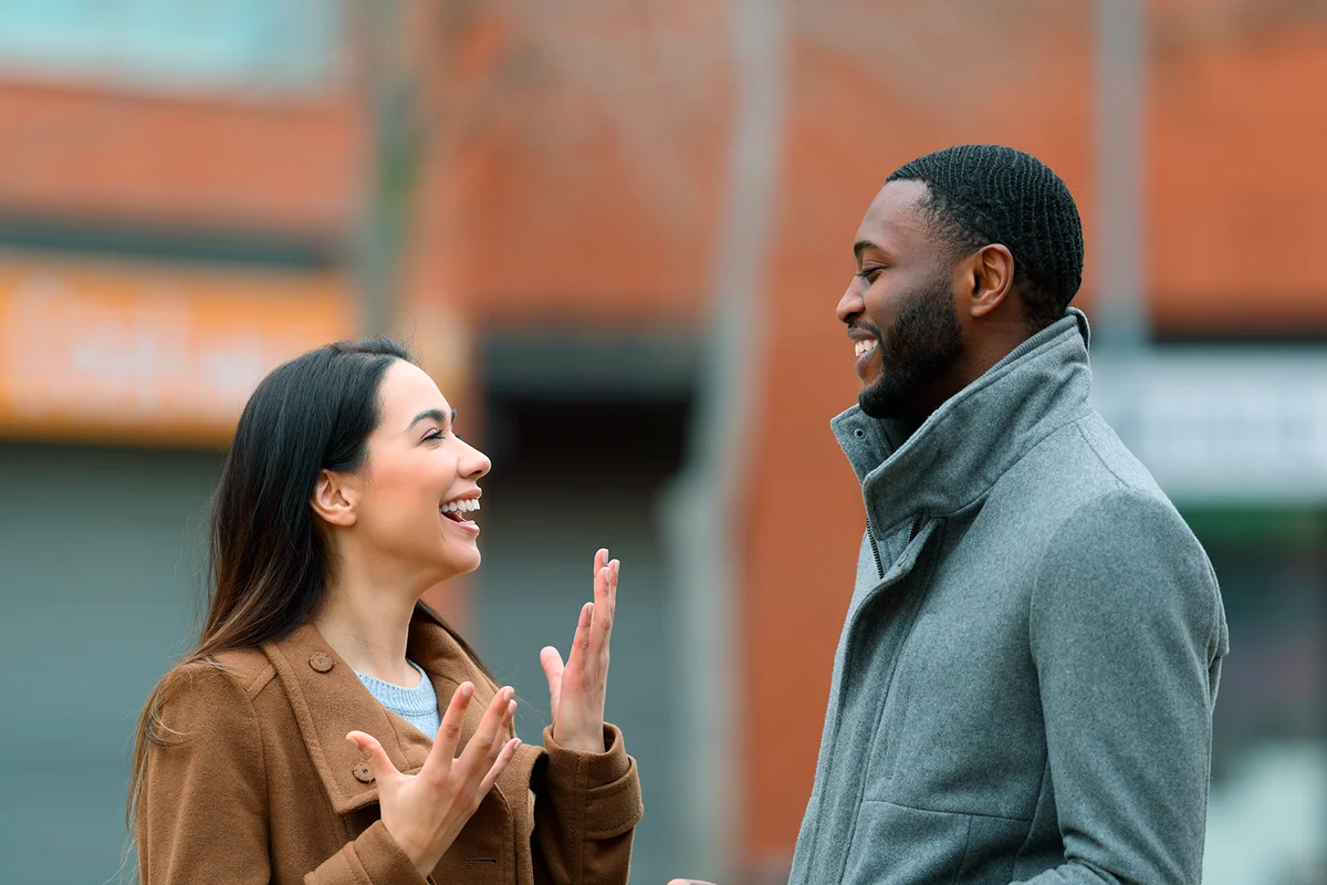 Side view portrait of a happy interracial relation with woman and man talking in the street
