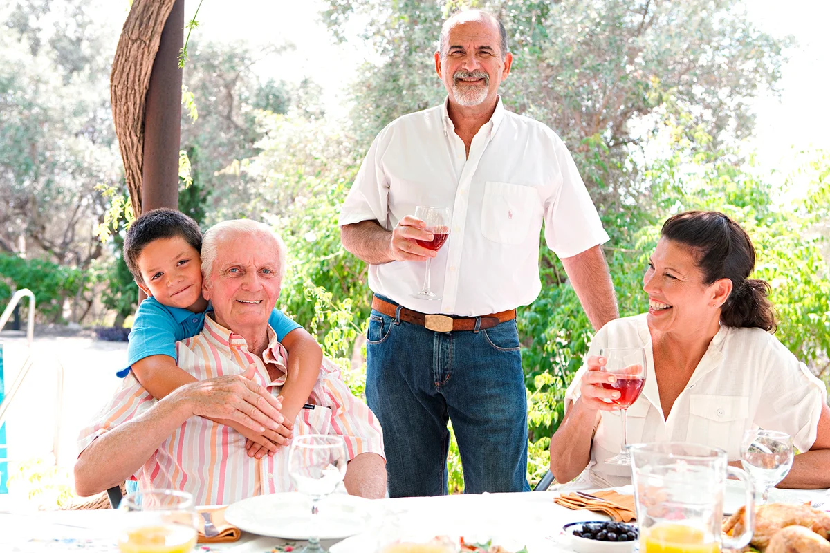 Portrait of a joyful family gathering around a healthy lunch food eating table outdoors during a summer holiday in a vacation garden home. Fun, love and affection family enjoying the sun, lifestyle