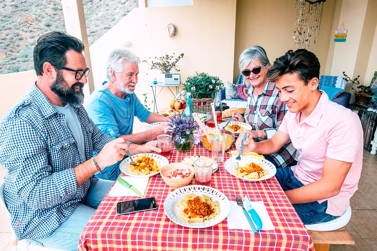 Family people outdoor lunch together on a red table - mixed ages generations enjoy and have fun with italian pasta on the terrace at home - father grandfather and son