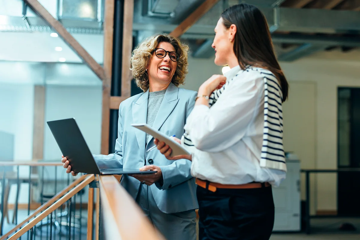 Business women smiling as they have a meeting on a balcony. Professional business women discuss their upcoming work and ways to get it done. Women working together in a female-led startup.