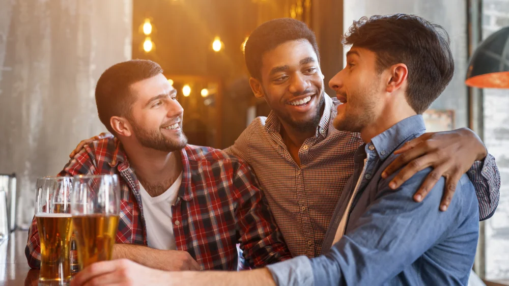 Group of three joyful best friends having enjoying beers in a bar