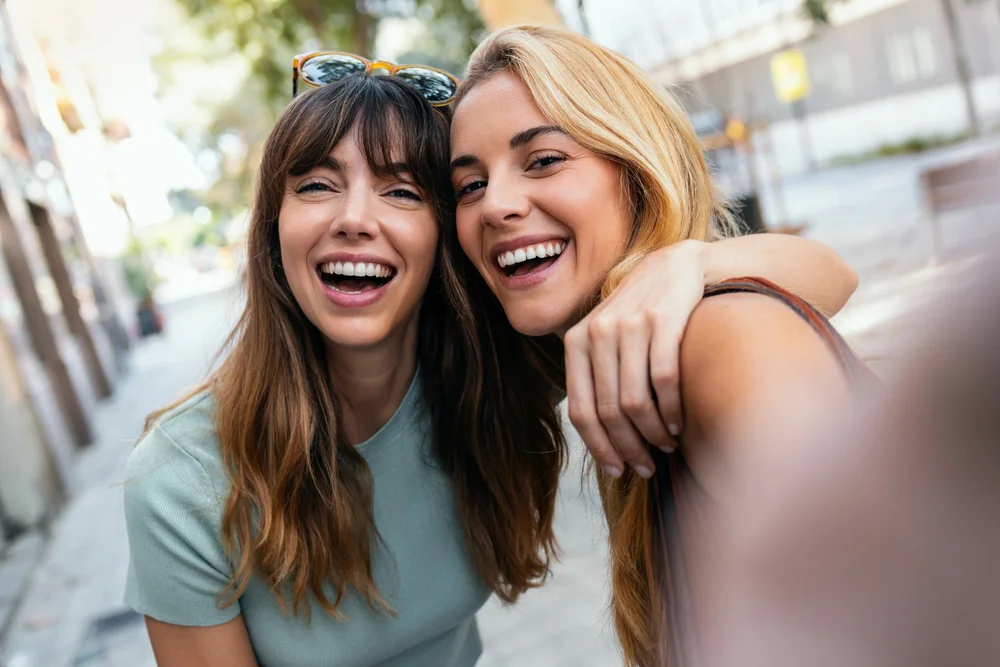 Two joyful woman taking a selfie in the city on a sunny day