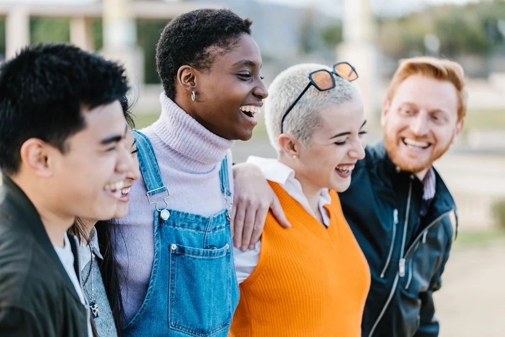 Group of happy multiracial friends hugging each other outdoors.