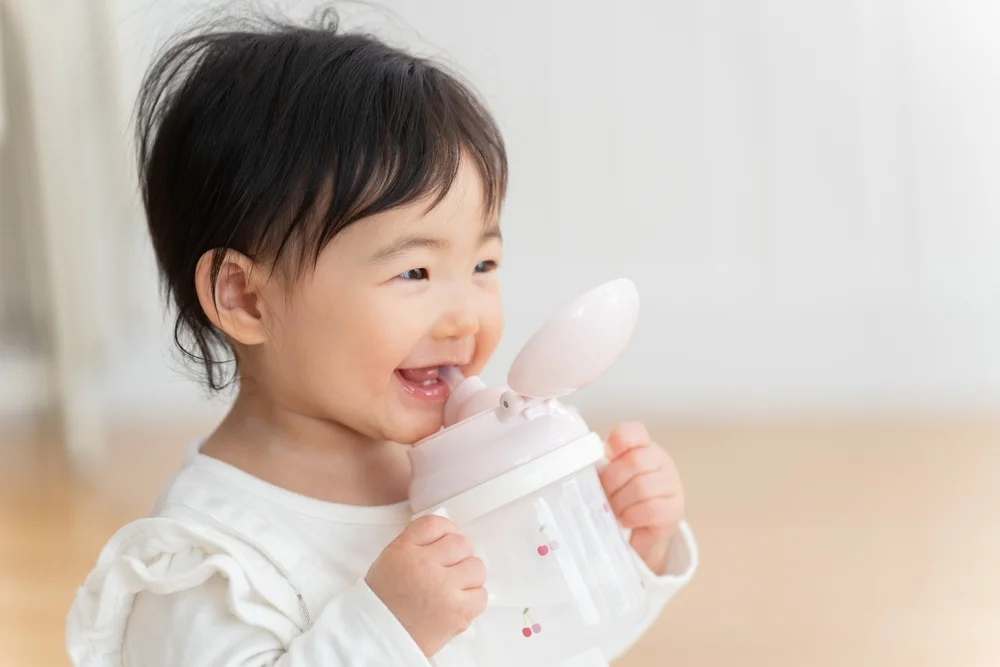 A 9-month-old asian baby girl drinking water from a mug