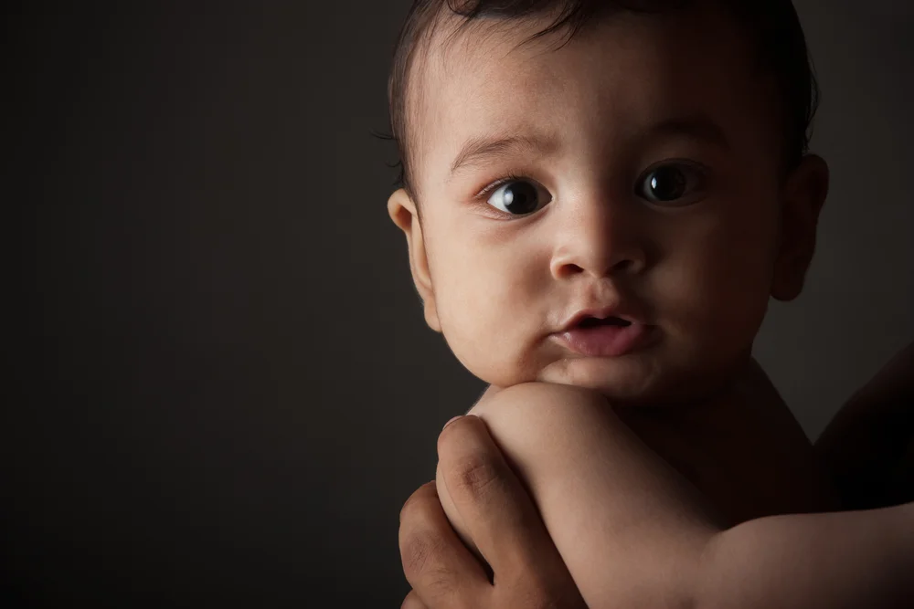 Close up portrait of an adorable indian baby boy in fathers arms on a black background