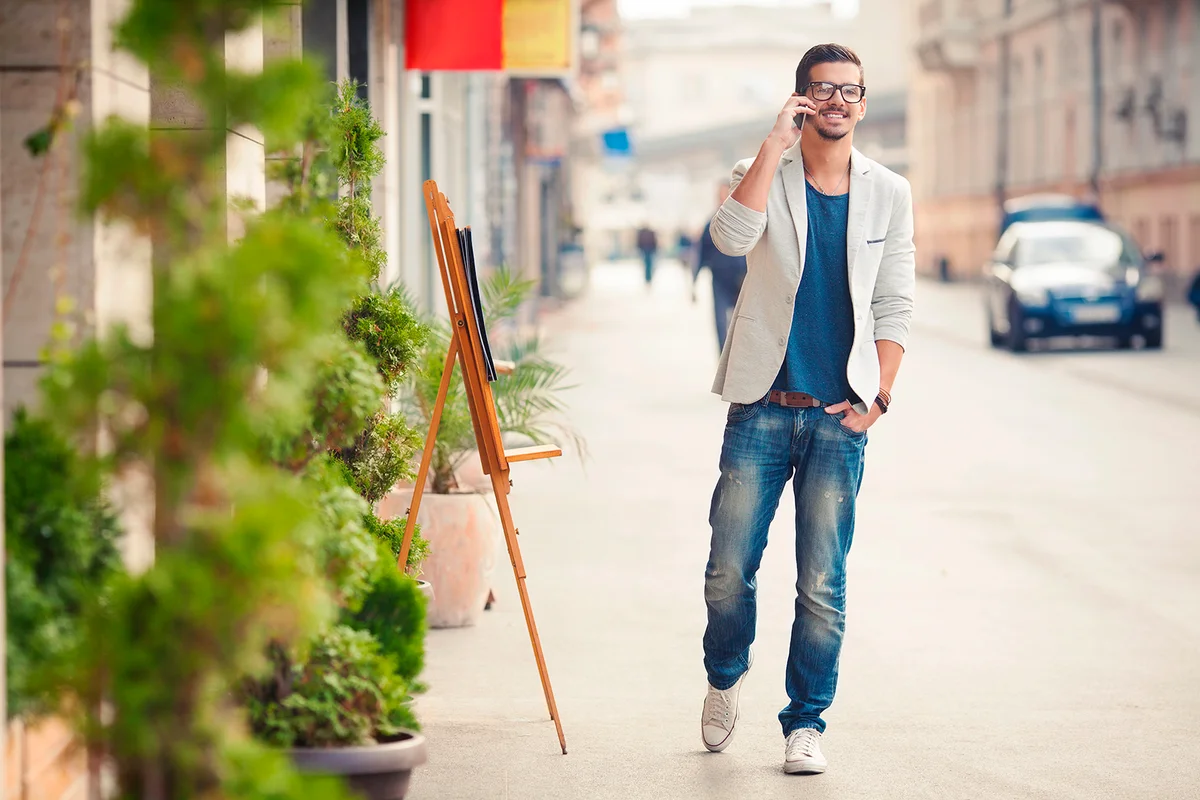 Handsome young man talking on the phone while walking on the street