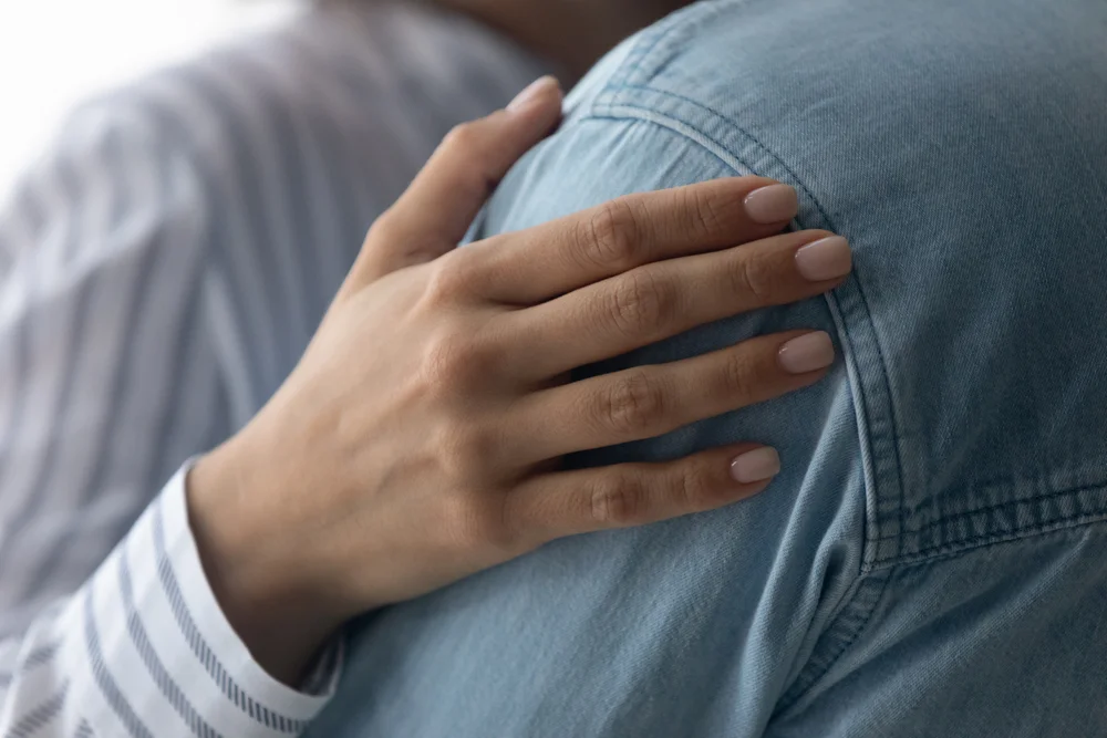 Caucasian woman's hand gently touching someone's shoulder