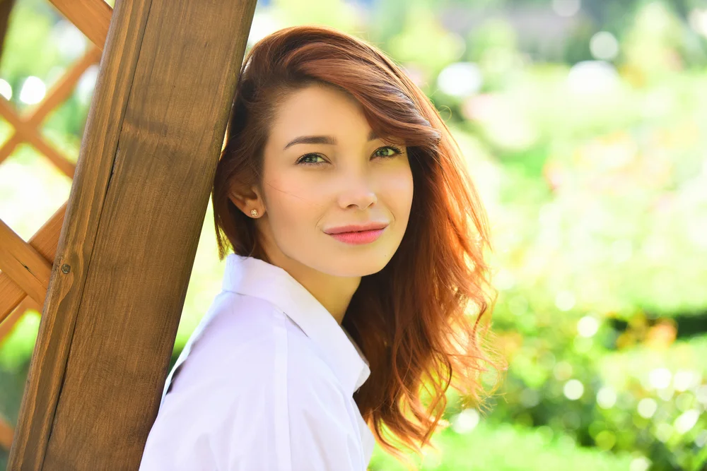 Close up portrait of a redhead beautiful woman standing in a garden looking at the camera