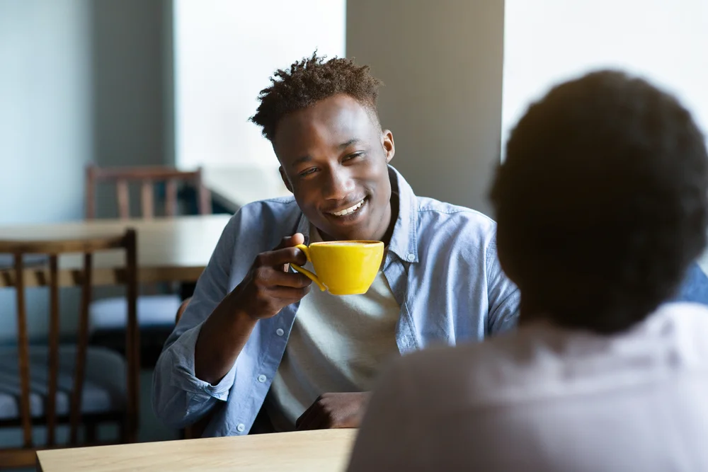 African-american man holds a cup while chatting with a friend in a coffee shop
