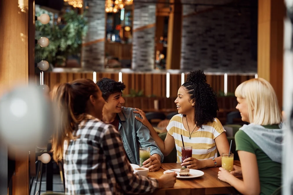 Diverse group of friends hanging out in a cafe, one of them talking directly to the friend by her side.