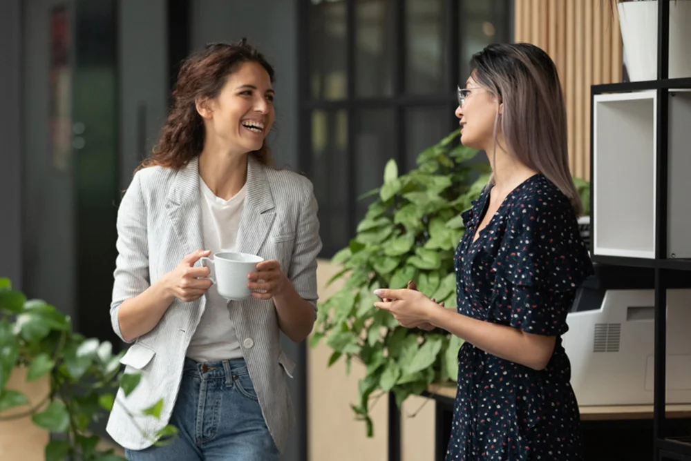 Happy female friends joking and laughing in a beautiful office cafeteria setting