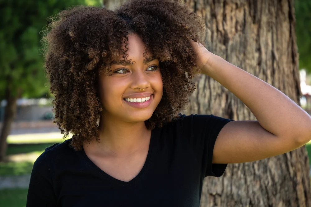 Beautiful African-american young woman smiling and touching her hair at the park